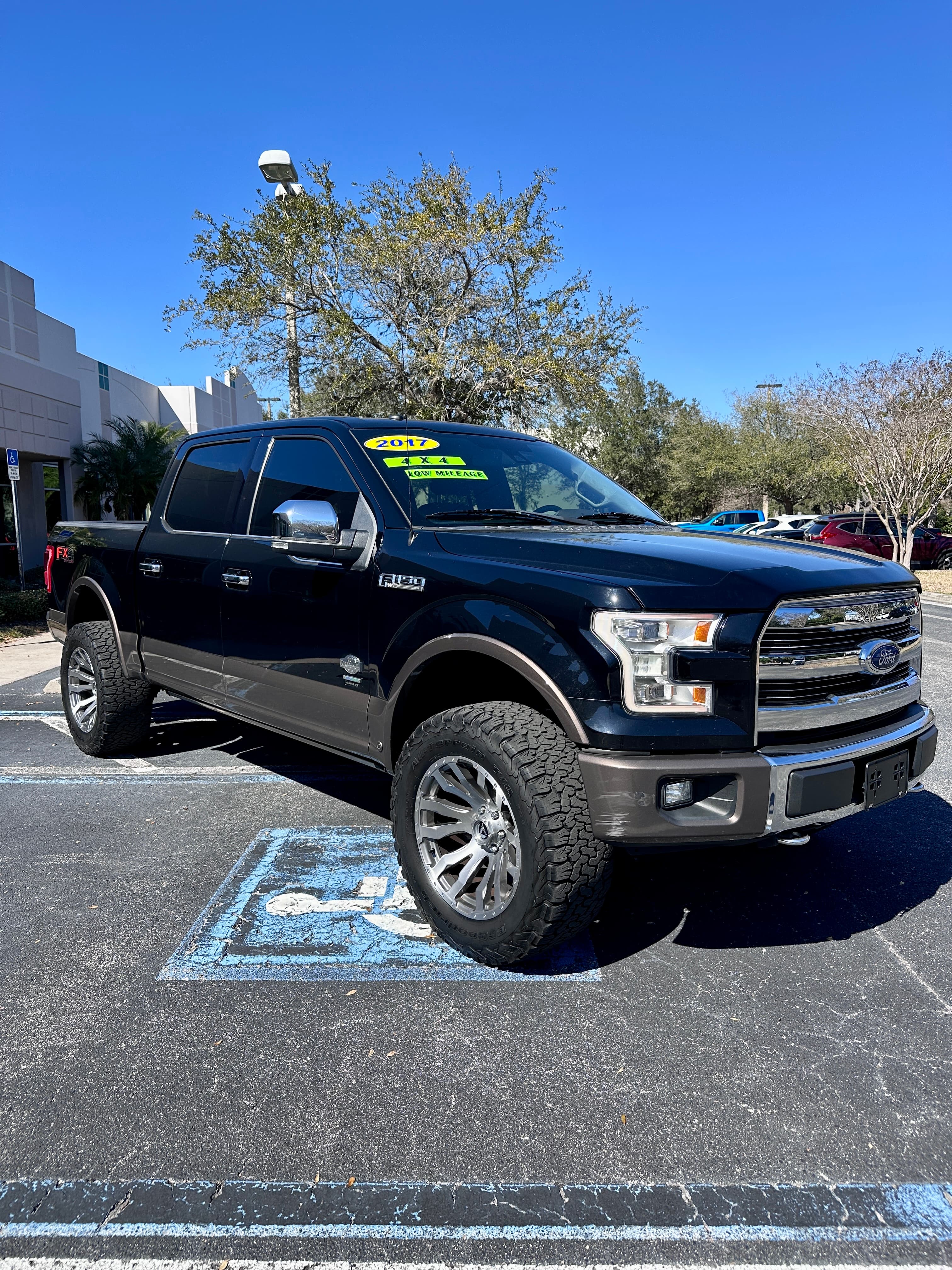 Black 2017 Ford F-150 4x4 pickup truck with off-road tires parked in a sunny lot.