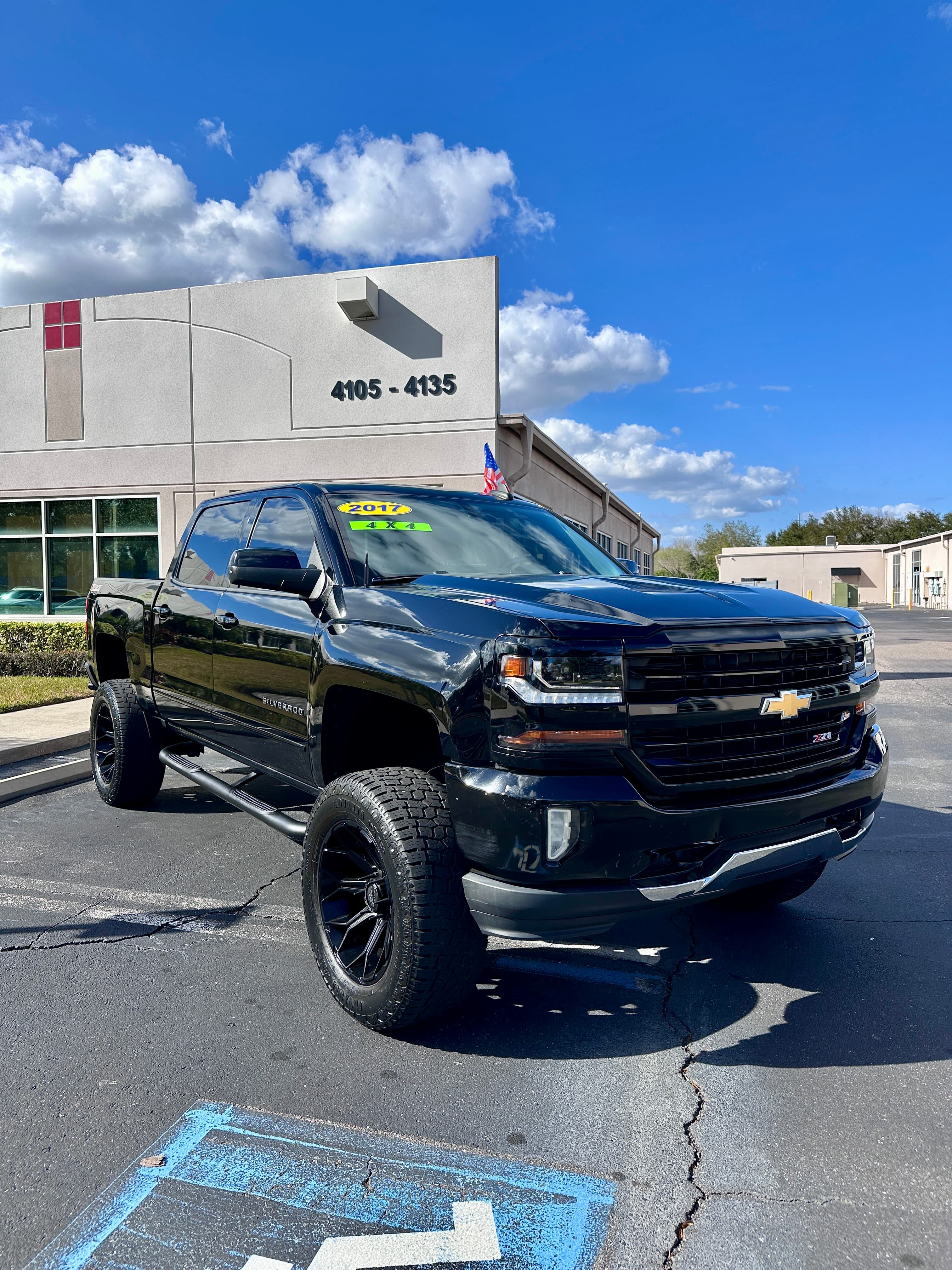Lifted black 2017 Chevrolet Silverado 4x4 truck parked in front of a commercial building.