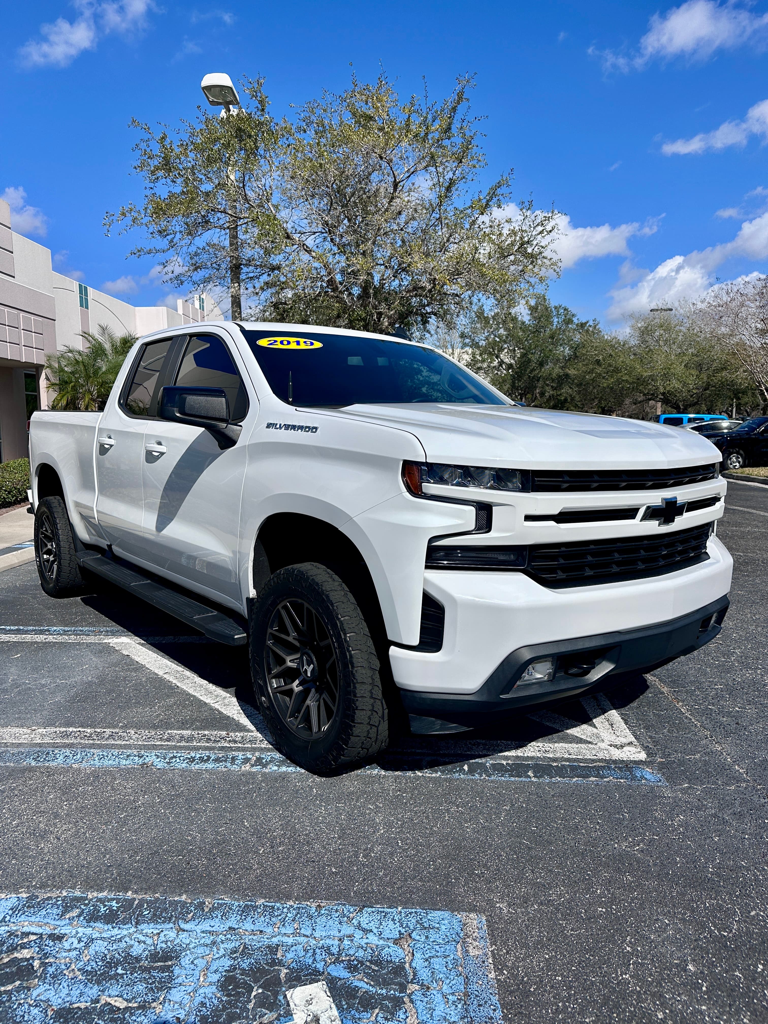 White 2019 Chevrolet Silverado pickup truck with black wheels parked in a sunny lot.