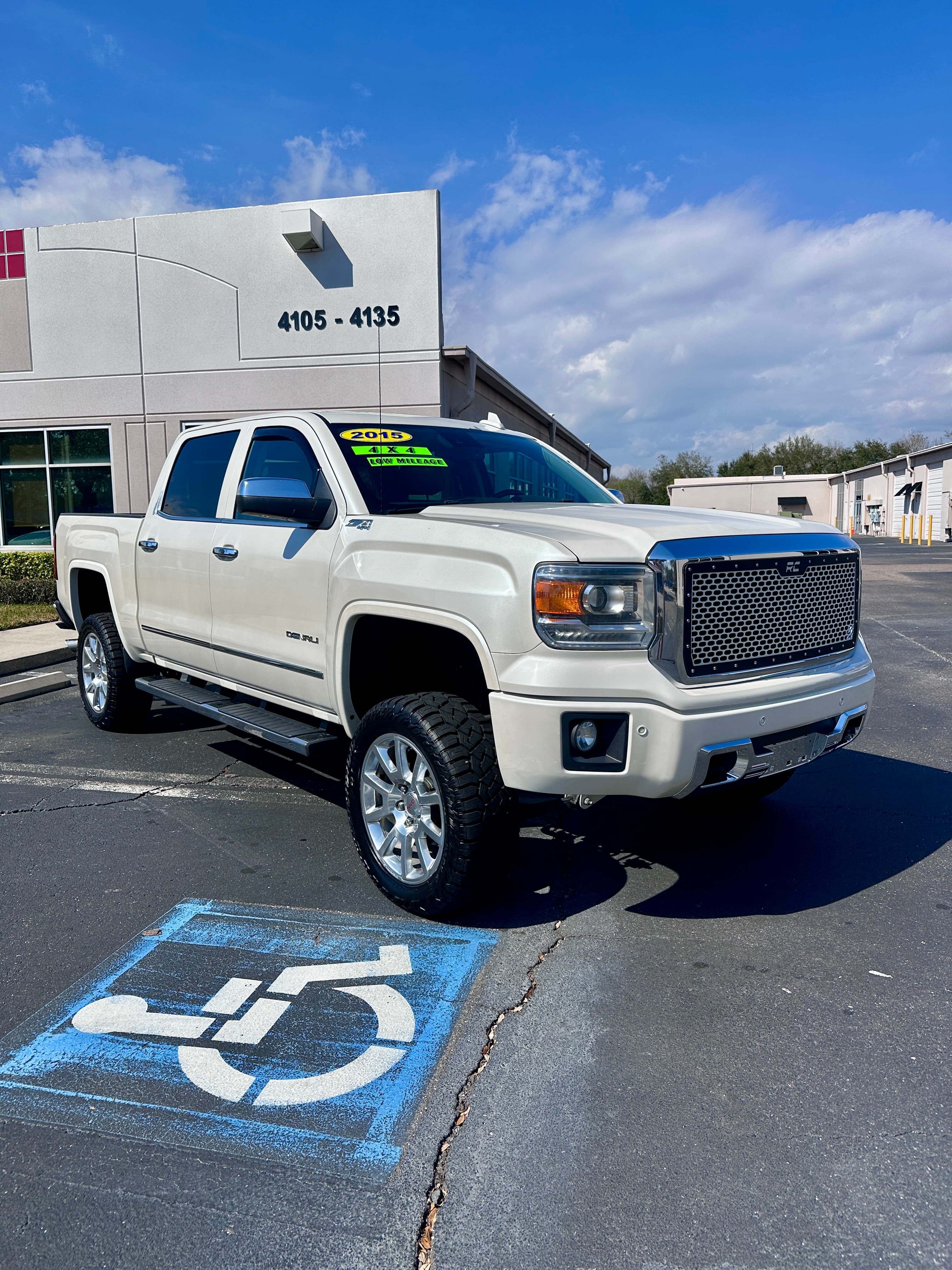 White 2015 GMC Sierra Denali lifted truck with off-road tires parked in a lot.