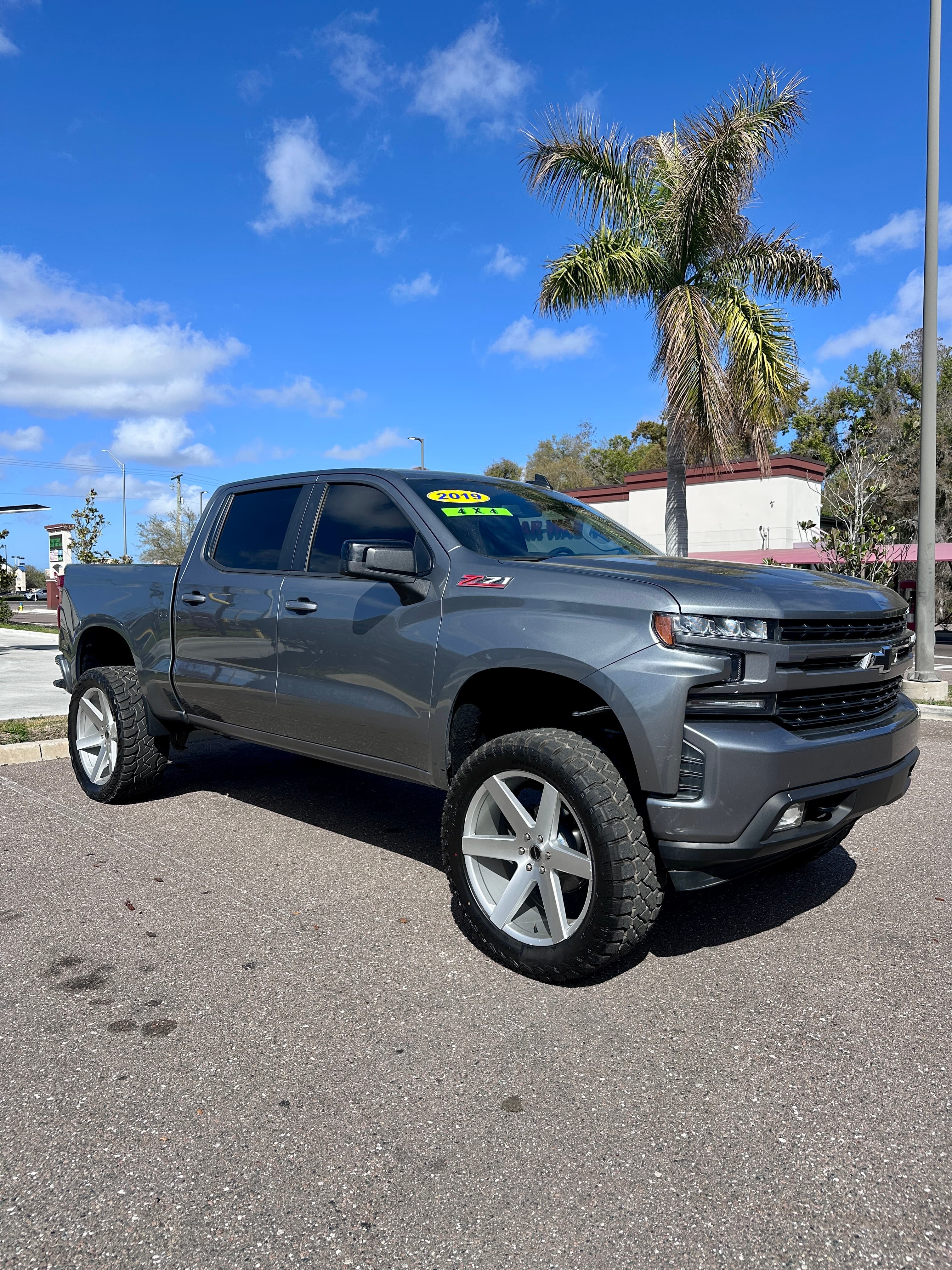 Grey lifted 2019 Chevrolet Silverado 4x4 truck with large silver wheels and off-road tires.