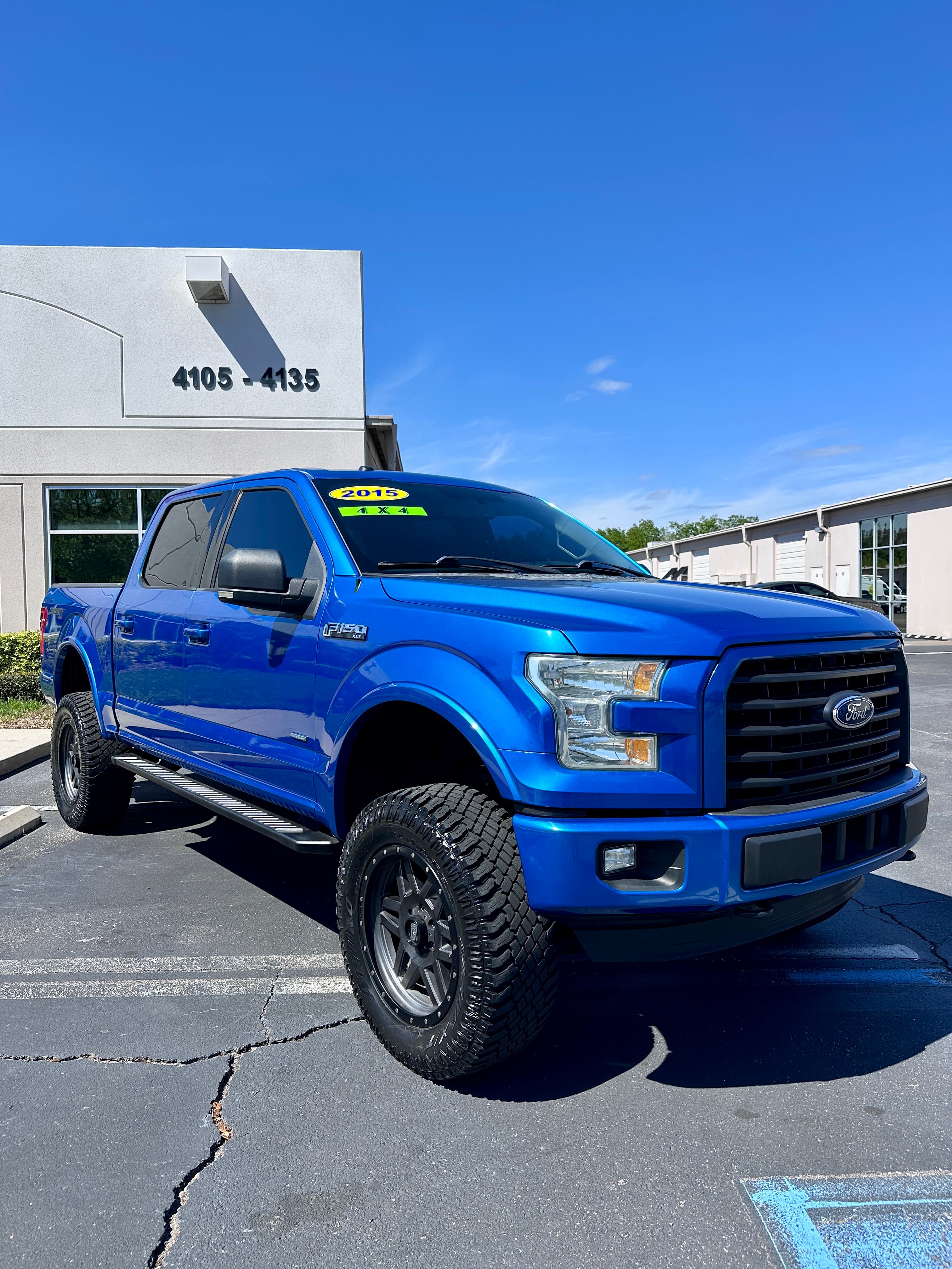 Lifted bright blue 2015 Ford F-150 pickup truck with large off-road tires and black wheels.