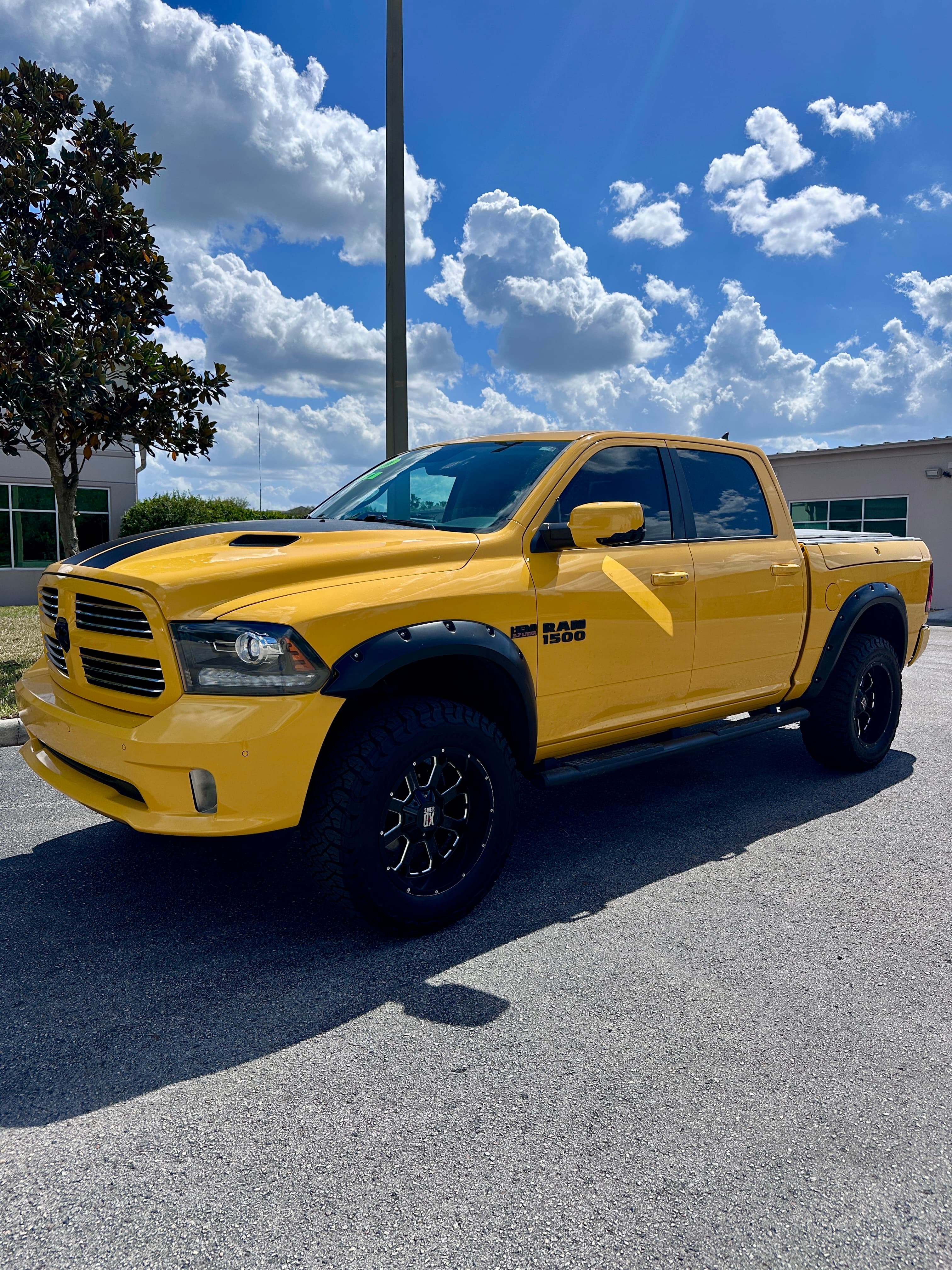 Bright yellow Ram 1500 pickup truck with black racing stripes and off-road tires.