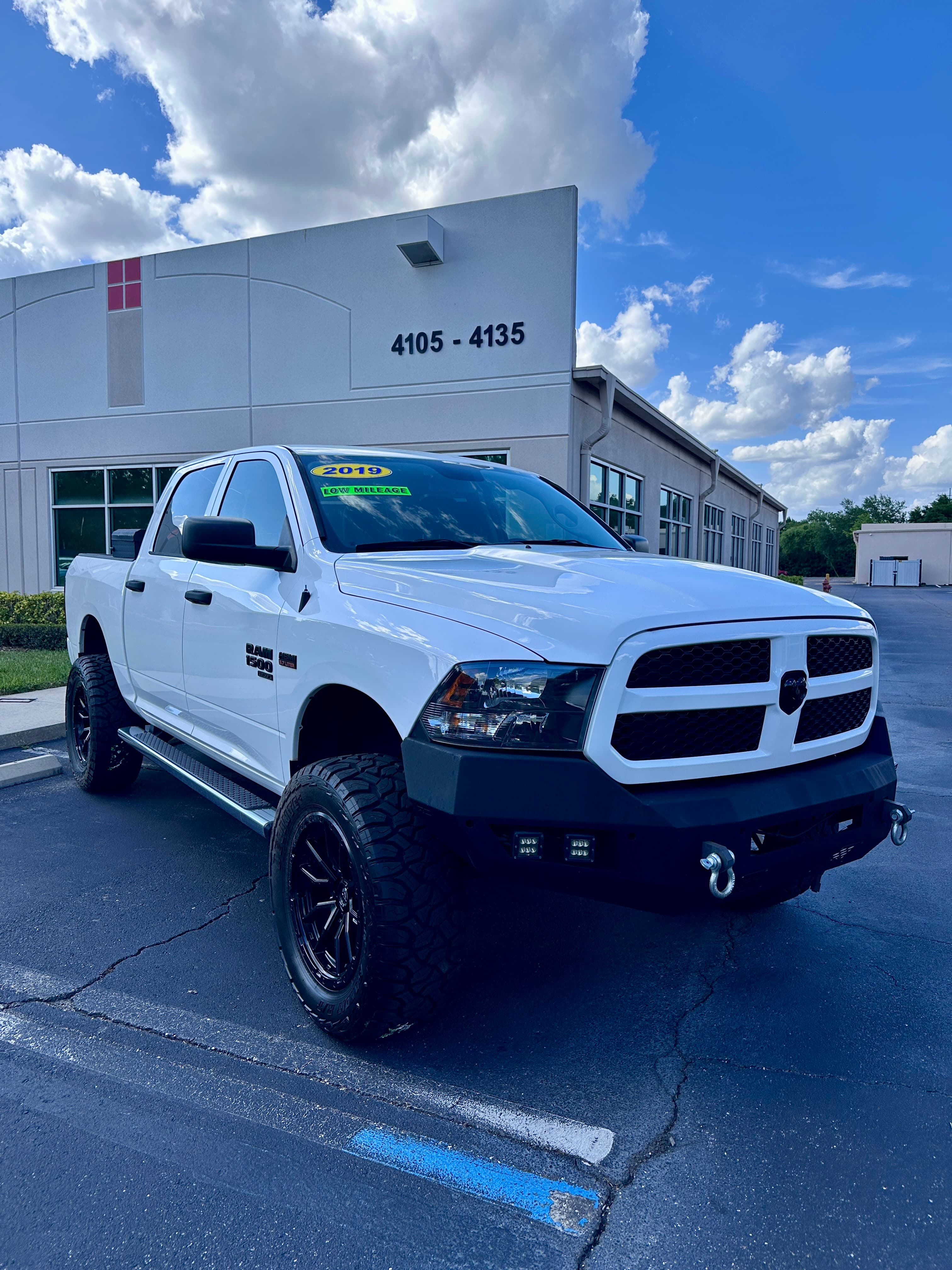 White lifted 2019 RAM 1500 pickup truck with black off-road wheels and a custom bumper.
