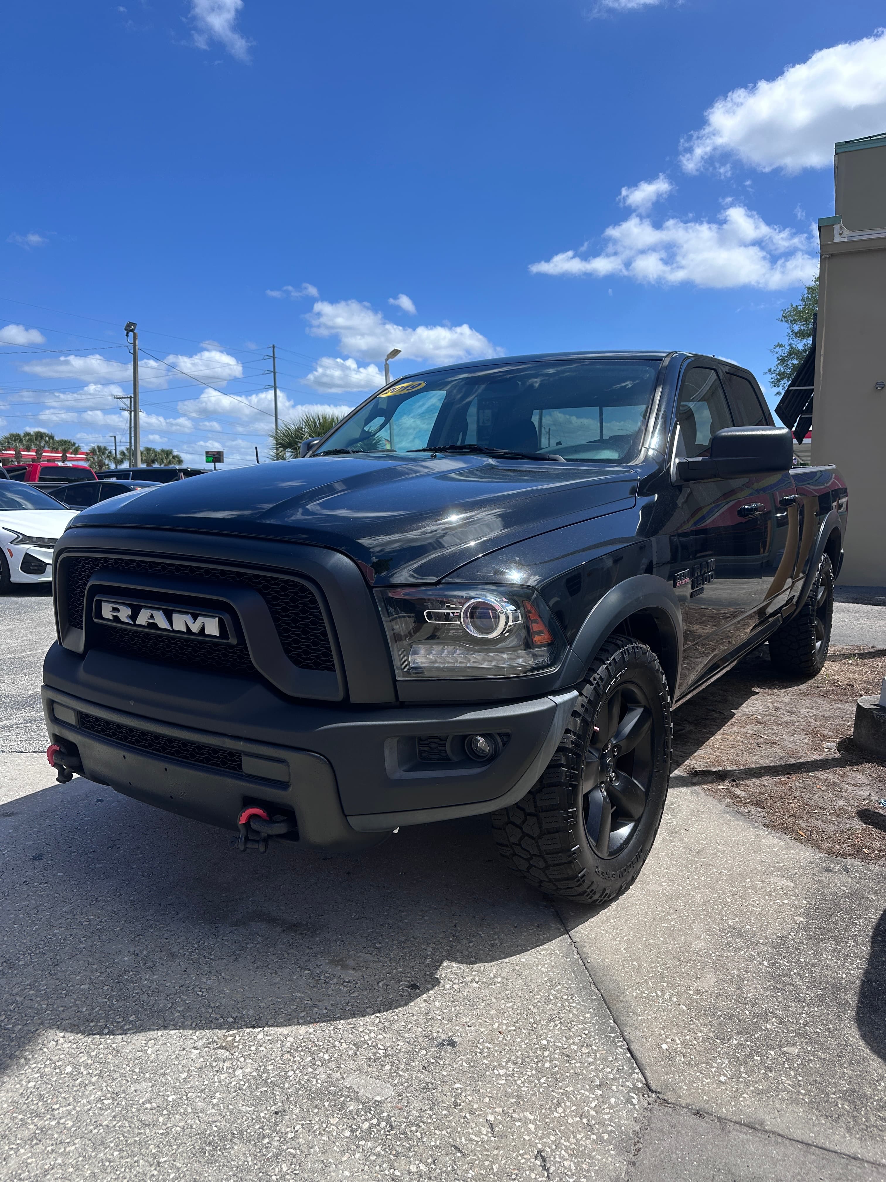 Black RAM pickup truck with off-road tires and red tow hooks under a blue sky.