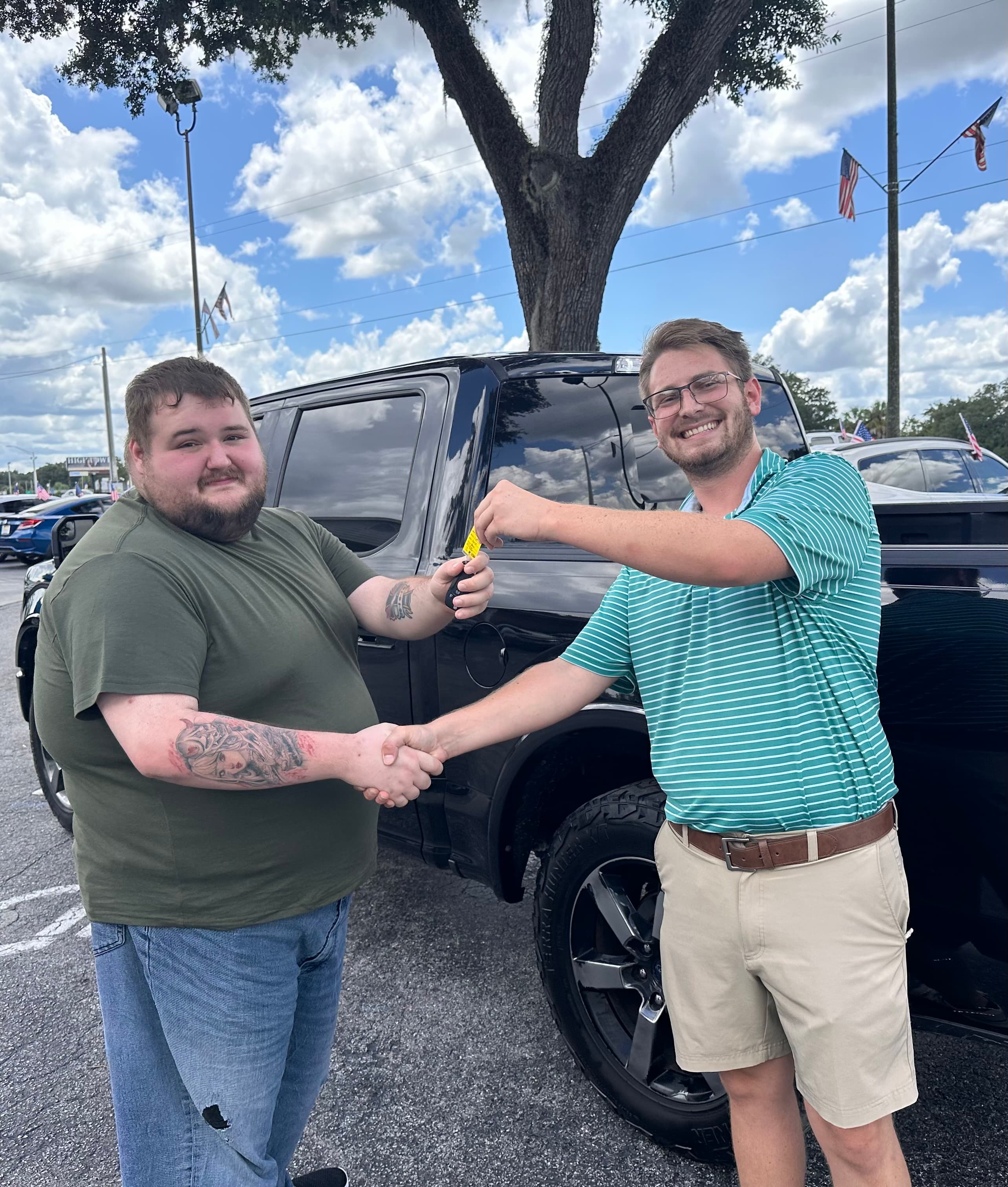 Two men shaking hands and exchanging car keys in front of a black pickup truck.