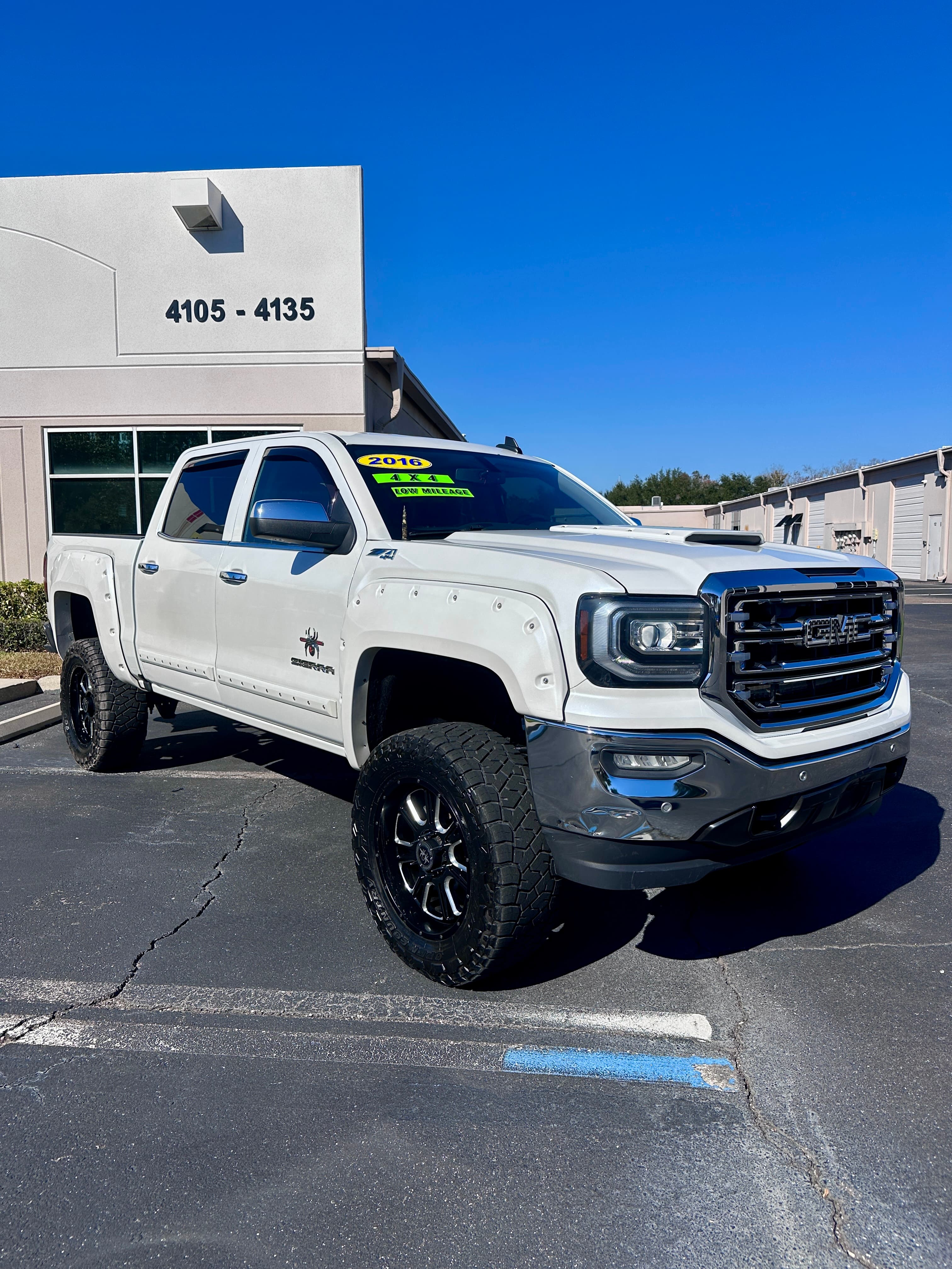 White lifted 2016 GMC Sierra 4x4 pickup truck with black wheels and off-road tires.