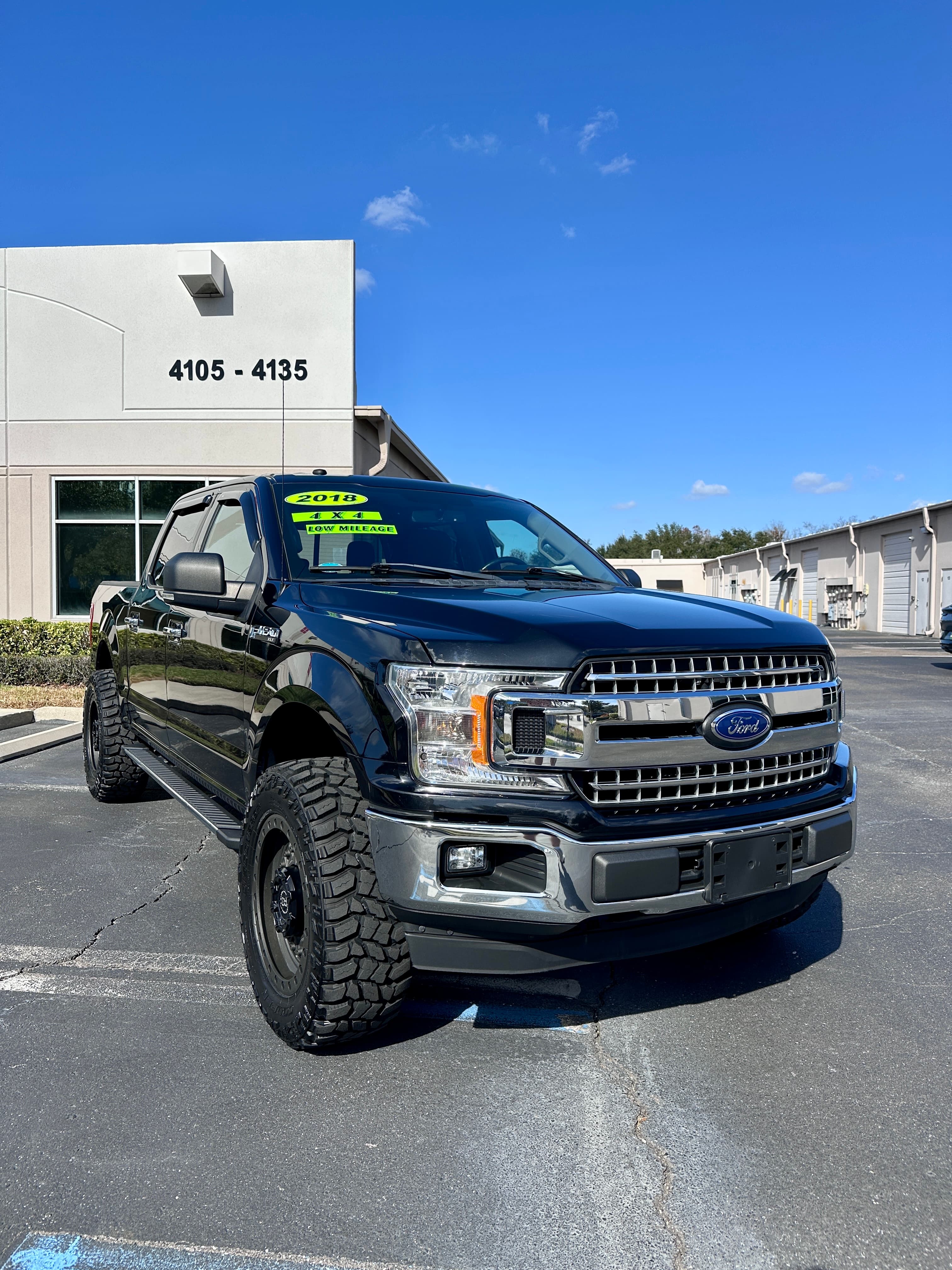 Black 2018 Ford F-150 pickup truck with off-road tires parked in a sunny lot.