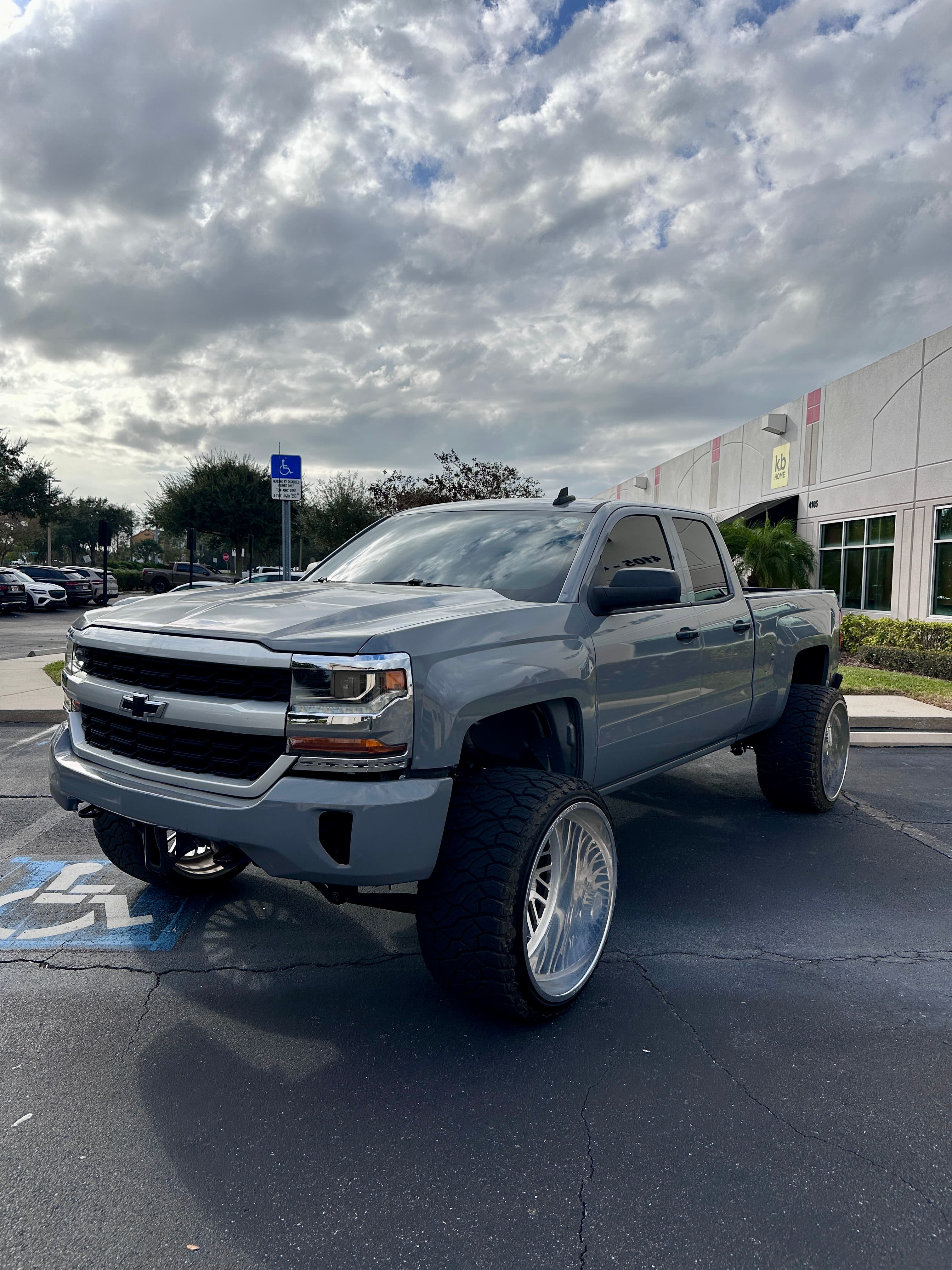 Grey lifted Chevrolet Silverado with massive deep-dish chrome wheels parked in a paved lot.