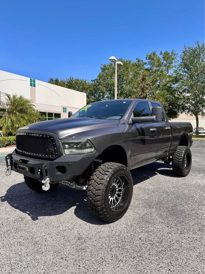 Lifted dark gray Ram pickup truck with large off-road tires and a custom front bumper.
